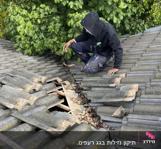 אדם בודק רעפים שבורים על גג עם עלים יבשים